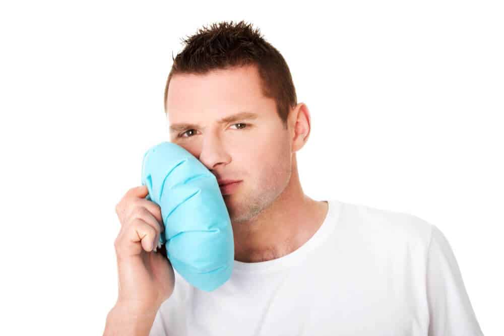 Person applying a cold compress to manage dental emergency pain before seeing a dentist